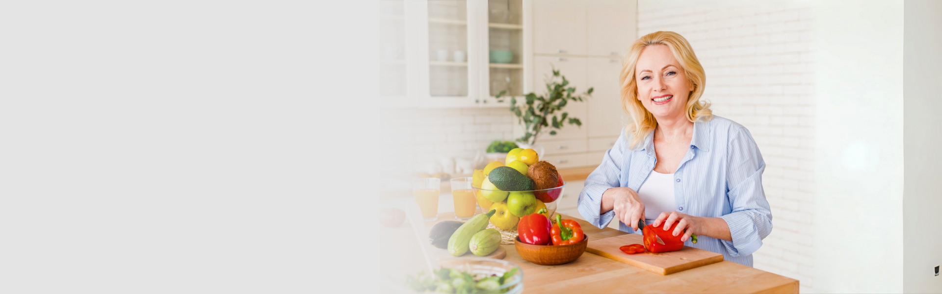 Smiling woman slicing red peppers at a kitchen counter set with fruit and vegetables