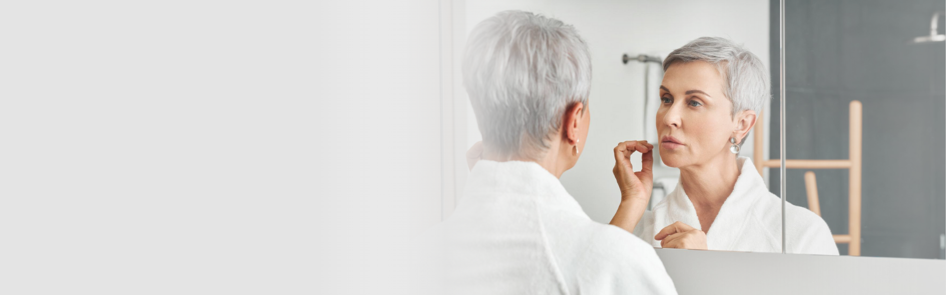 Woman with short silver hair looking at her reflection in a bathroom mirror