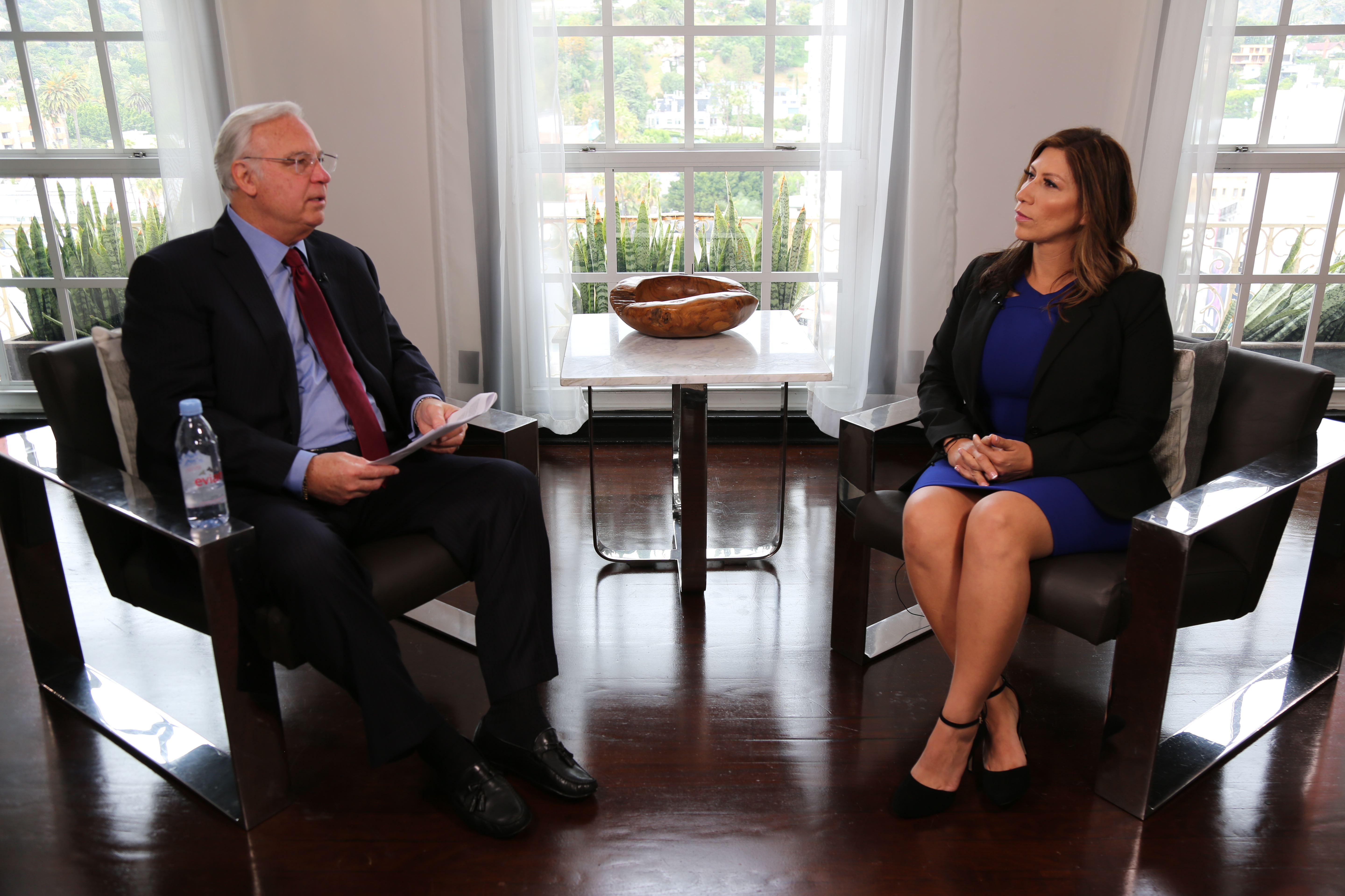 Maria Martinez seated opposite an interviewer in front of tall windows