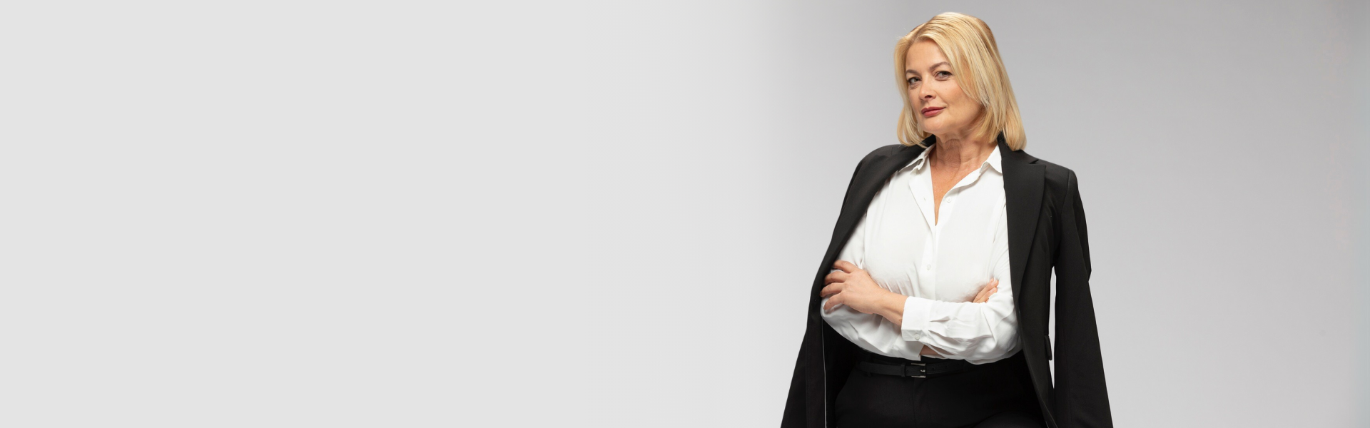 Woman in a black blazer and white shirt standing with her arms folded